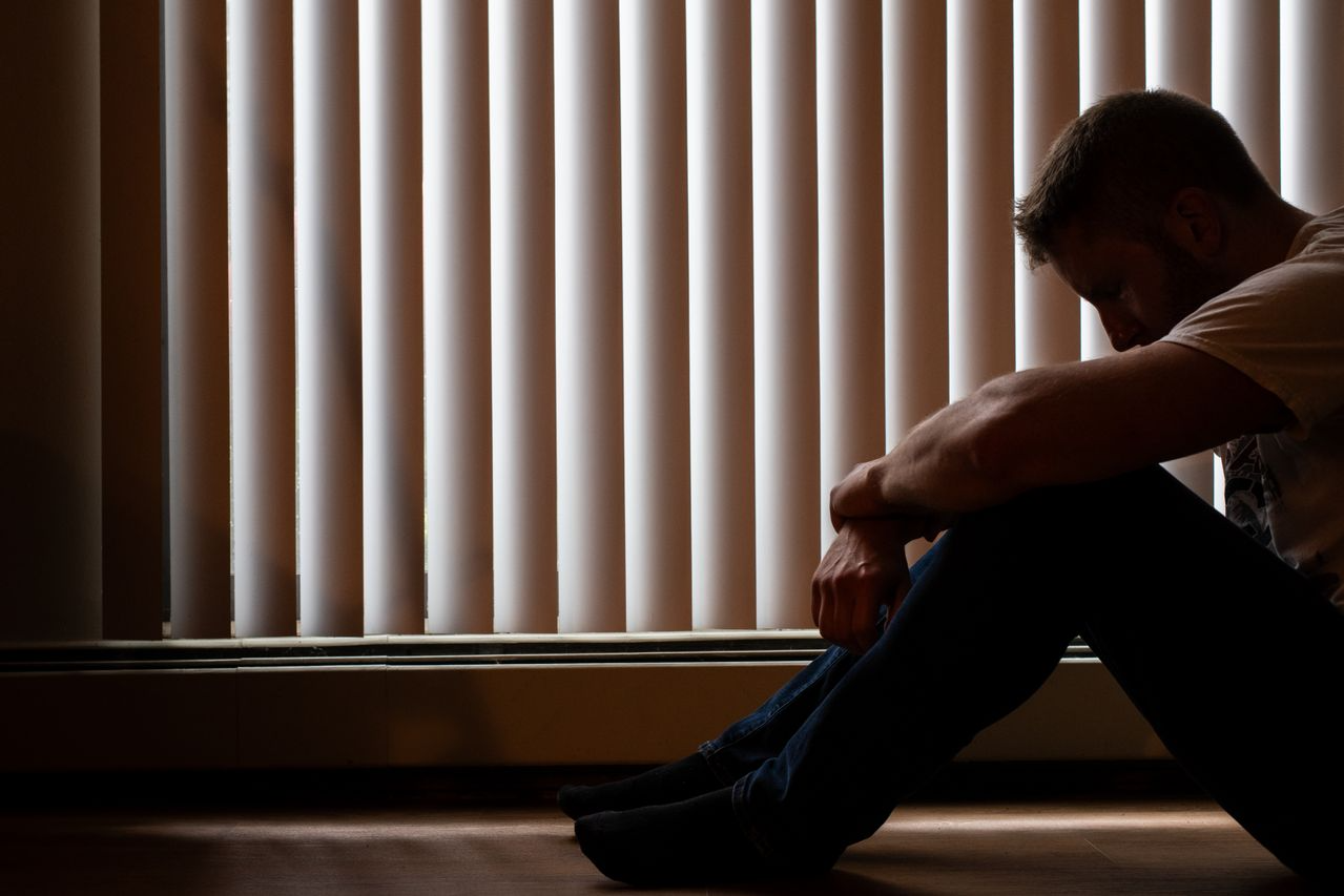 homem com a cabeça baixa em ambiente escuro, representando fatores emocionais relacionados ao que causa a depressão.
